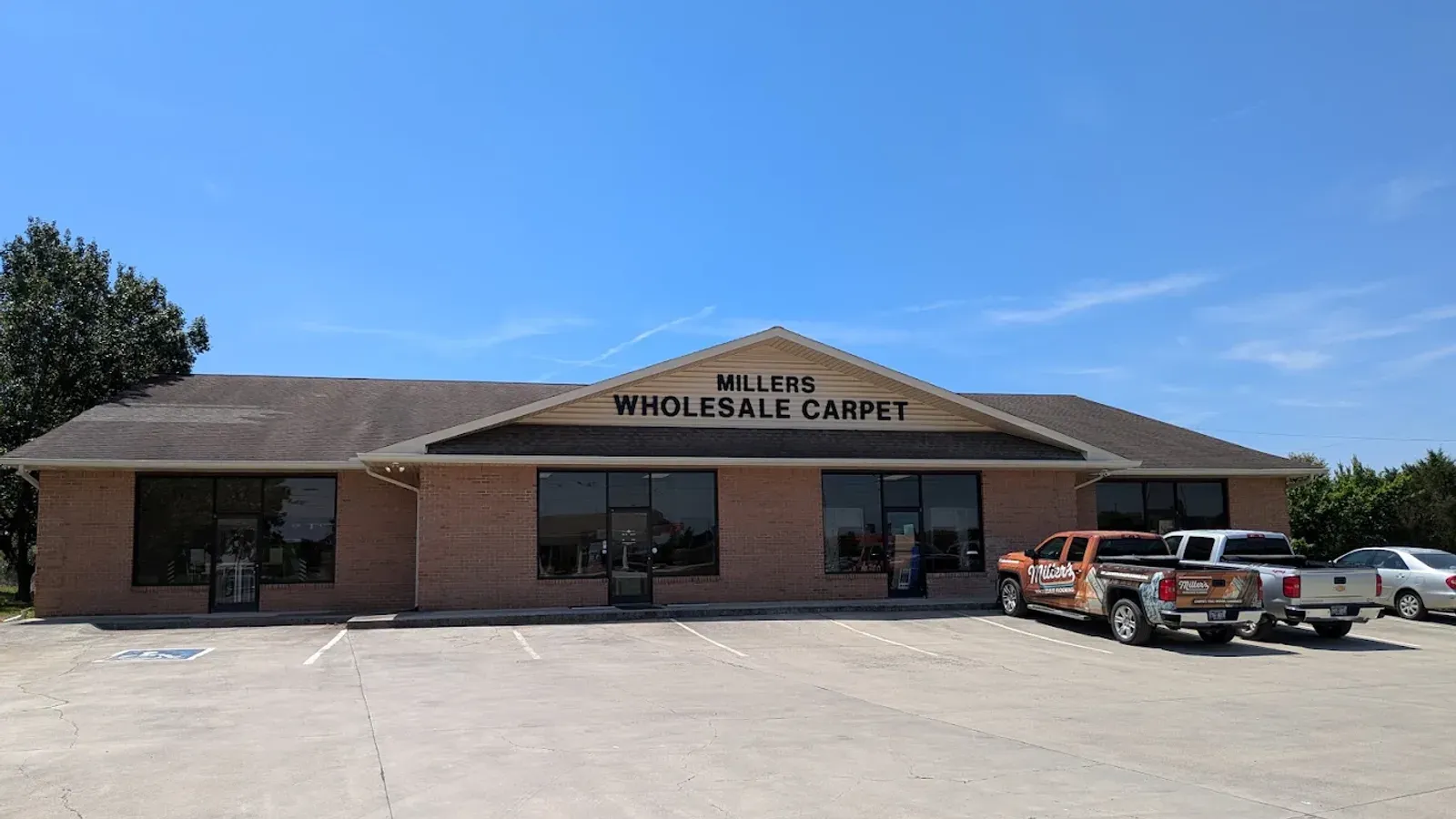 The Miller's storefront in Madisonville, Tennessee with the original Millers Wholesale Carpet sign over the entrance and two Miller's-wrapped work trucks parked out front